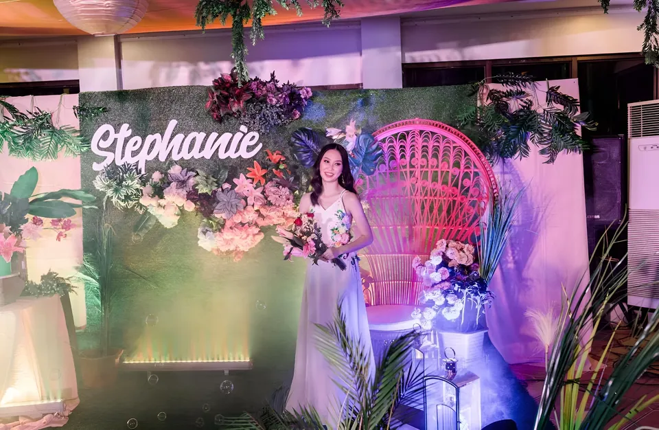 Stephanie Jean King in white gown holding bouquet in front of floral backdrop