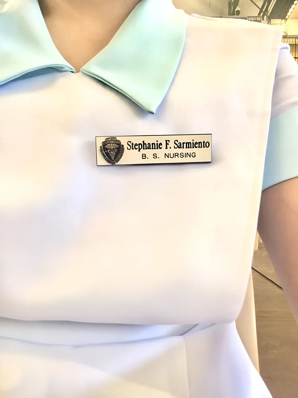 Stephanie Sarmiento — A close-up photo shows a white garment with a light blue collar and name badge