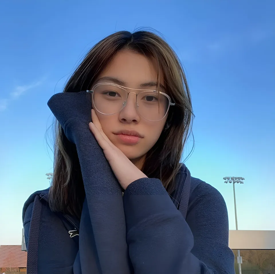 Thea Herrera in blue hoodie poses with hand near face outdoors