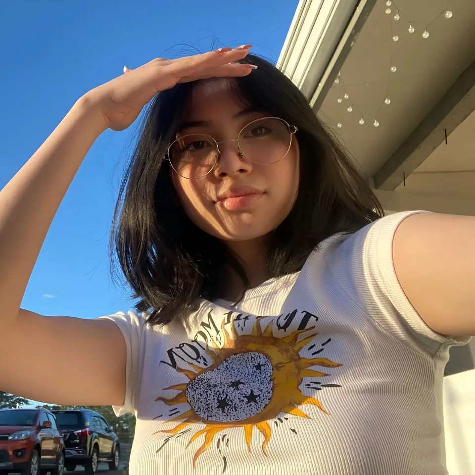 Thea Herrera wearing white t-shirt with sun graphic, shielding eyes from sun