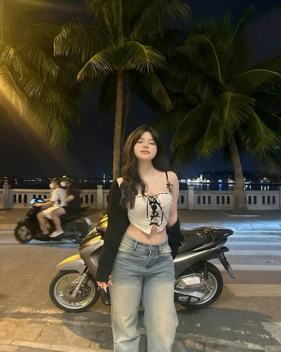 Yue Arden standing beside scooter under palm trees at night