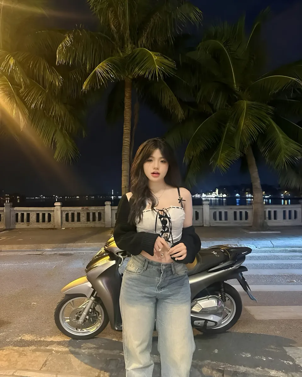 Yue Arden standing beside scooter under palm trees at night