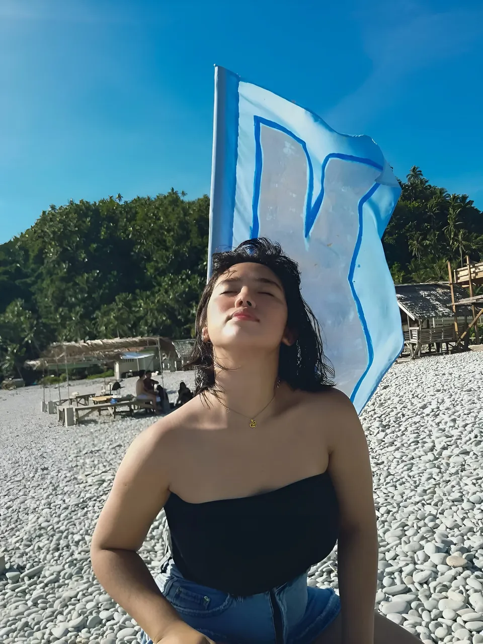Zianne Tremedal seated on pebbled beach with flag behind them