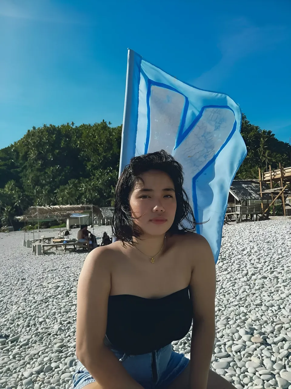 Zianne Tremedal in black top seated on pebble beach with flag behind