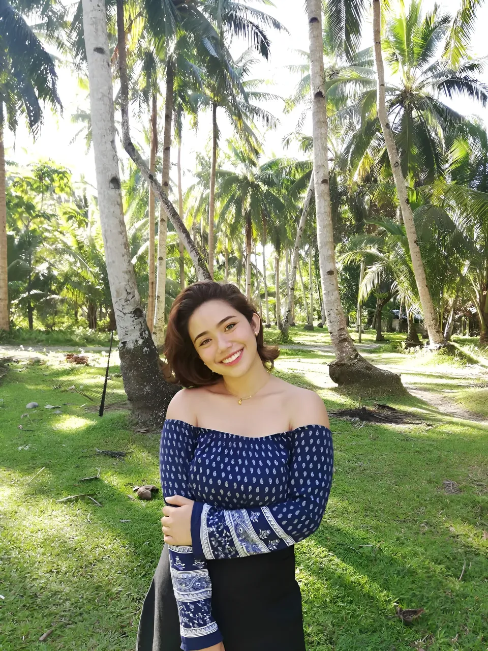 Zianne Tremedal in blue patterned top standing outdoors among palm trees